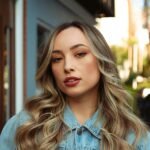 A fashionable woman with curly hair wearing a denim shirt outdoors.